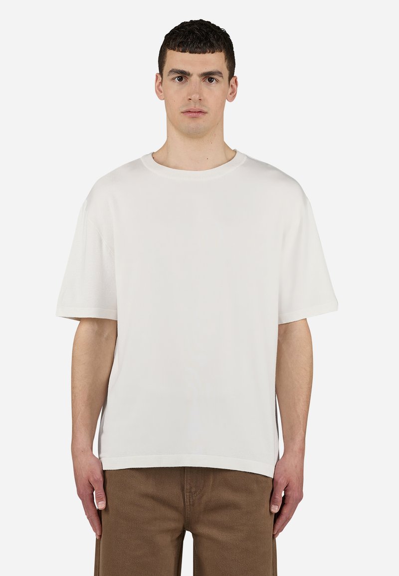 White, short-sleeve t-shirt with a round neckline and relaxed fit, made of soft, smooth fabric; pairs with brown pants.