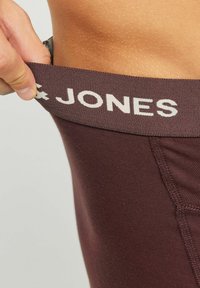 Burgunderfarbener Bund mit "JONES"-Logo; eng anliegendes Textilmaterial; glatte Textur; heruntergezogener Bund, der den darunter liegenden Stoff zeigt.