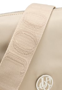 Borsa a mano in nylon beige con tracolla testurizzata caratterizzata da cerchi in rilievo e dettaglio del logo in metallo. Chiusura con zip nella parte superiore.