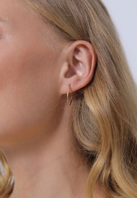 Boucles d'oreilles en or avec un design fin et allongé, suspendues de manière sécurisée au lobe de l'oreille. Texture lisse, finition réfléchissante et style minimaliste.