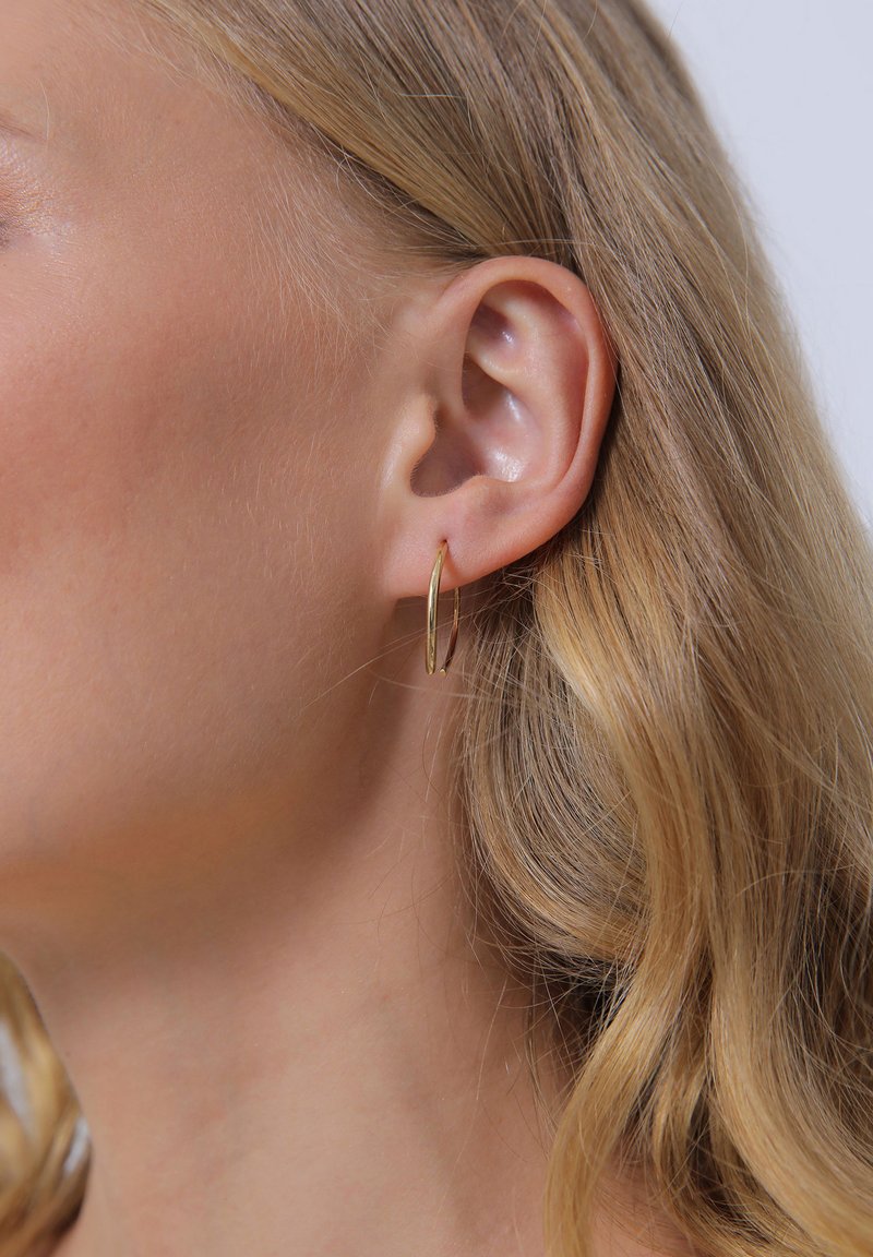 Boucles d'oreilles en or avec un design fin et allongé, suspendues de manière sécurisée au lobe de l'oreille. Texture lisse, finition réfléchissante et style minimaliste.