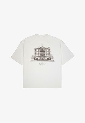 White cotton t-shirt featuring a detailed brown architectural illustration of a building on the back, with the text "Palace Grand Resort" below.