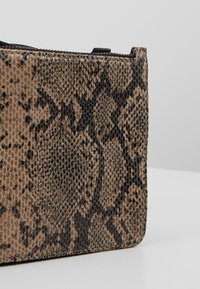 Primo piano di una borsa texturizzata con un motivo a stampa pitone marrone e nero, con una cerniera lungo il bordo superiore su uno sfondo chiaro.