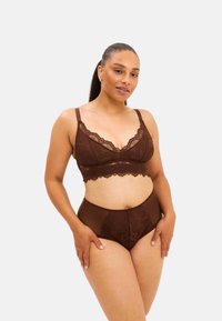 Ruskea pitsinen bralette, jossa on aaltoilevat reunat ja ohuet säädettävät olkaimet, yhdistettynä korkeavyötäröisiin ruskeisiin pitsireunaisiin alushousuihin. Sujuva pinta.