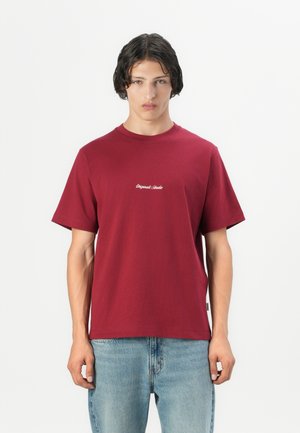 Bordeaux kortlopende katoenen t-shirt met een ronde hals en subtiele geborduurde logo op de borst. Gecombineerd met lichtblauwe denim jeans.