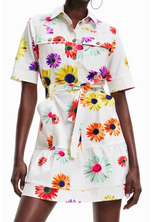 Weißes Kleid mit Gürtel, bunten großen Blumenmustern, kurzen Ärmeln, geknöpften Brusttaschen, getragen von einer Person mit dunkler Haut.