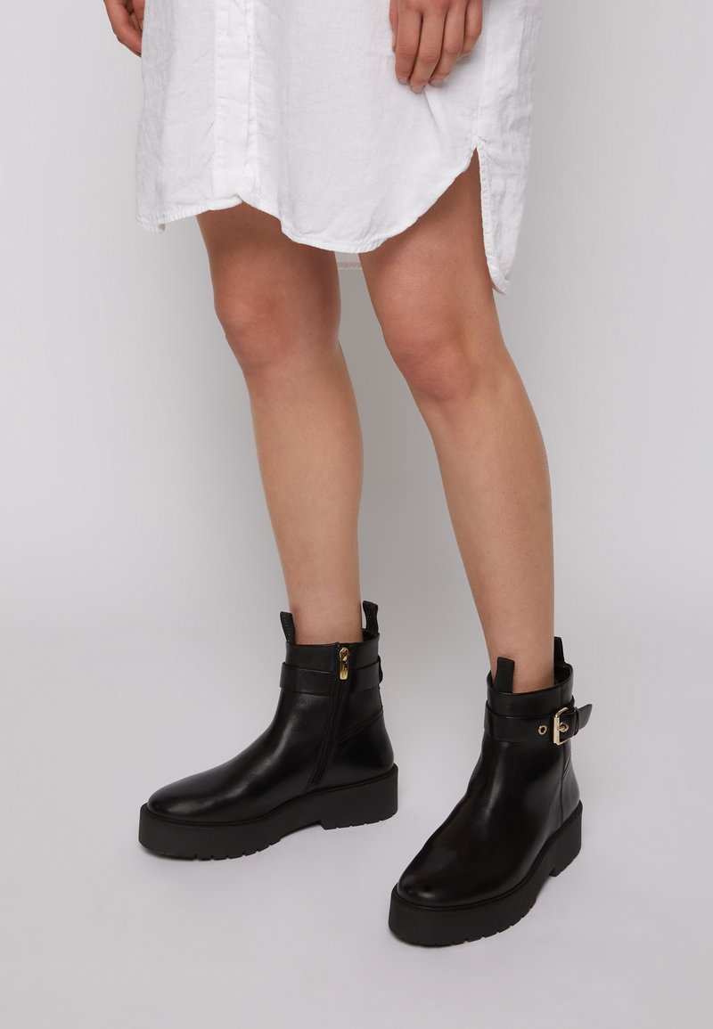Czarne skórzane botki za kostkę z masywną podeszwą, zamkiem błyskawicznym i szczegółami pasa. Gładka tekstura, elegancki design i zaokrąglony nosek.