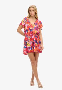 Romper floreale di un vivace rosso, con maniche corte, scollatura a V, vita cinchata e fondo svasato con una leggera texture del tessuto.