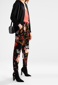 Svarta blommiga byxor med röda, rosa och vita blommor, i kombination med en korallfärgad topp och en svart blazer. Svarta anklarstövlar med knappar.