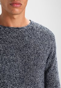 Marineblauer Strickpullover mit einem strukturierten, wellenförmigen Muster. Verfügt über einen Rundhalsausschnitt und lange Ärmel. Hergestellt aus einem weichen, leichten Material.
