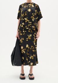 Robe noire florale avec une silhouette ample, dotée de manches courtes, d'un col froncé et de motifs floraux jaunes pâles. Associée à des sandales noires et à un sac.