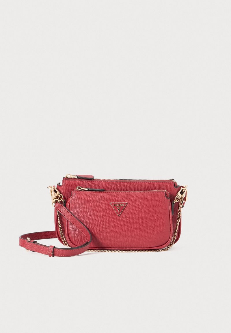 Sac bandoulière rouge avec bandoulière chaîne dorée, fermetures zippées et logo triangular Guess sur le devant, présenté sur un fond blanc uni.