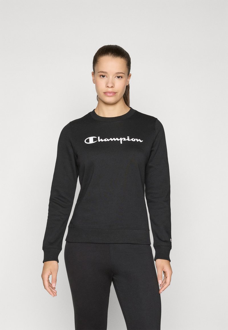 Zwarte sweater met lange mouwen, ronde halslijn en een opvallend wit "Champion" logo over de borst. Zacht, textuurstof.