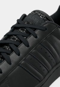 Μαύρο δερμάτινο αθλητικό παπούτσι με υφαντές λεπτομέρειες στη γλώσσα, επίπεδα κορδόνια και τρεις διάτρητες ρίγες. Διαθέτει ομαλή, υφή επιφάνεια.