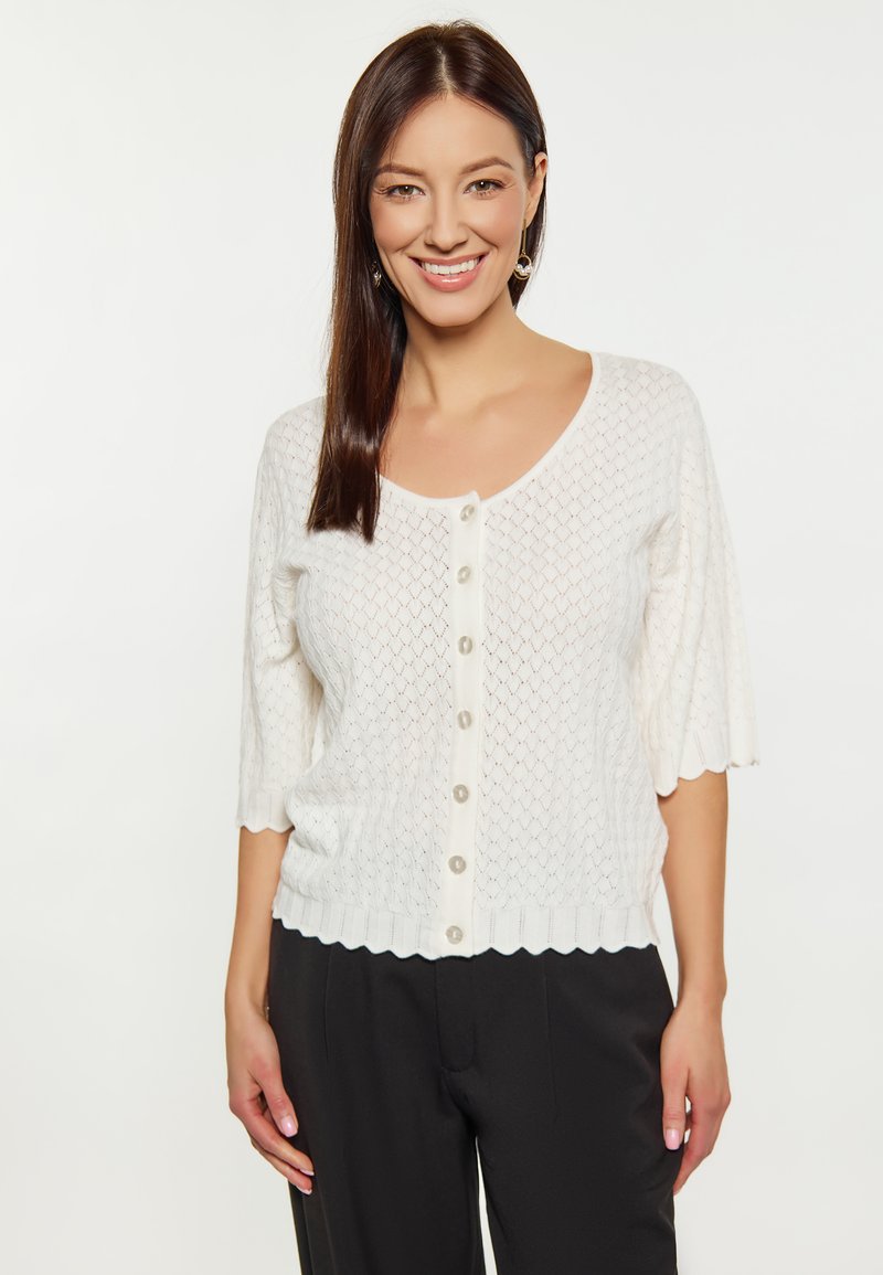 Cardigan bianco lavorato a maglia con maniche a 3/4, orlo scallop e bottoni al centro. Presenta un motivo a rombi e una texture morbida.