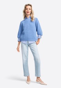 Maglione azzurro chiaro lavorato a maglia con una finitura testurizzata, abbinato a una camicia a righe bianche e blu, jeans in denim chiaro e décolleté bianche con punta.