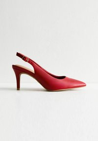 Röd läder slingback-högklackad sko med spetsig tå, guldspänne och en slät yta på en ljus bakgrund.