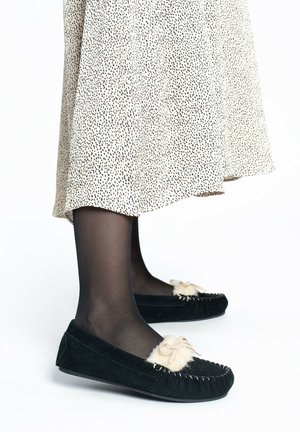 Zapatillas de ante negro con acentos de piel de pelo y un detalle de lazo. El diseño presenta una punta redondeada y costuras decorativas a lo largo de los bordes.