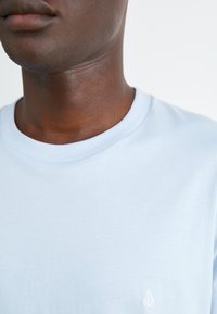 Világoskék pamut póló bordás kerek nyakkivágással és kicsi fehér logóval a bal oldalon. Puha tapintás és egyszerű dizájn.
