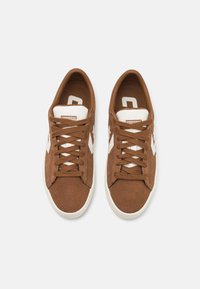 Kahden ruskeiden samettisten Converse-tennareiden, joissa on valkoiset kumipohjat, valkoinen kielilappu ja valkoinen nuoli- ja tähtilogo sivuilla.