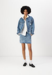 Τζάκετ από τζιν με ανοιχτό πλύσιμο και μπροστινές τσέπες, συνδυασμένο με φούστα από τζιν της ίδιας απόχρωσης. Λευκό πουκάμισο με κουμπιά από κάτω. Μαύρες λόφερ και λευκές κάλτσες.