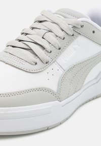Baskets Puma blanches et gris clair en cuir texturé, lacets tissés et logo Puma en relief sur le panneau latéral, gros plan.