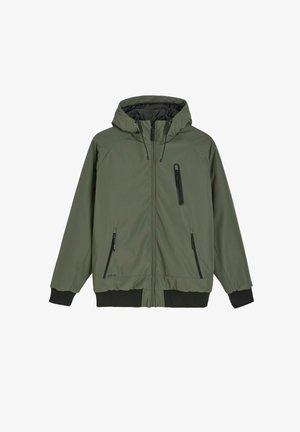 Oliwkowa kurtka z kapturem, z przednim zamkiem błyskawicznym, dwoma bocznymi kieszeniami na zamek i jedną kieszenią na zamek na piersi. Ma ribbowe mankiety i dół. Gładka tekstura.