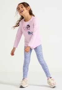 Ljusrosa långärmad tröja med en paljettfjärilsdesign, kombinerad med blå leggings med blommönster och ljusa sneakers med detaljer.