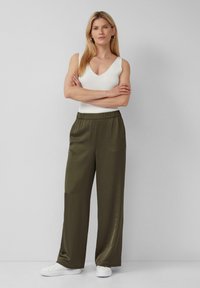 Olivgrüne weit geschnittene Hose aus einem glatten Material mit einem elastischen Bund. Kombiniert mit einem figurbetonten, weißen ärmellosen Top und weißen Schuhen.