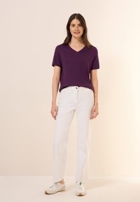 Fialové tričko s krátkým rukávem a výstřihem do V v kombinaci s bílými kalhotami rovného střihu a světlými teniskami, s jednoduchým designem a hladkou texturou.