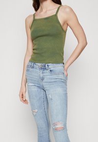 Camiseta verde de canalé con tirantes finos, combinada con jeans skinnies descoloridos de color azul claro con detalles rasgados y un diseño clásico de cinco bolsillos.