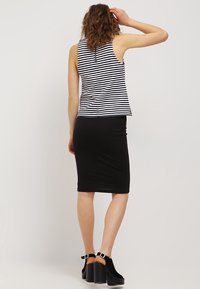 Falda lápiz negra combinada con una blusa sin mangas a rayas en blanco y negro. La blusa tiene un corte holgado y un escote alto. Zapatos de tacón grueso.