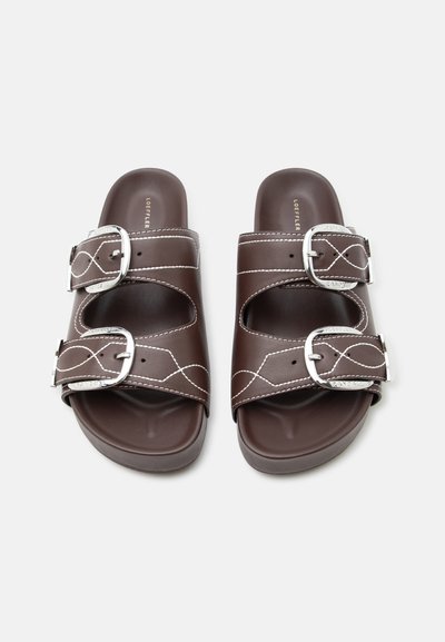 Καφέ δερμάτινα σανδάλια slide με διπλές ασημένιες αγκράφες και λευκή ραφή στις λουρίδες, επίπεδη σόλα, από πάνω.