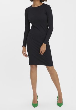 Schwarzes, geripptes Kleid mit langen Ärmeln, figurbetonte Silhouette, oberschenkellang, kombiniert mit grünen High Heels. Glatte Textur, schlichtes Design.