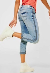 Svetle modré džíny z denimu s přiléhavým střihem, ohrnutými manžetami a dekoračním prošitím. Kombinované s bílými vysokými teniskami.