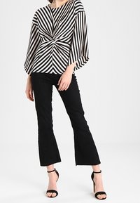 Musta-valkoiset raidalliset yläosa, jossa on kierretty etuosan muotoilu, yhdistetty mustiin leveisiin housuihin. Yläosassa on leveät hihat ja pehmeä kangas.