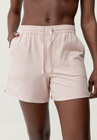 Ružové, ľahké šortky s elastickým pásom a šnúrkou; obsahujú bočné vrecká a hladký povrch.