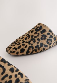 Chaussures slip-on à imprimé léopard en fausse fourrure texturée avec un bout pointu et une semelle noire, présentant des taches noires irrégulières sur un fond beige.