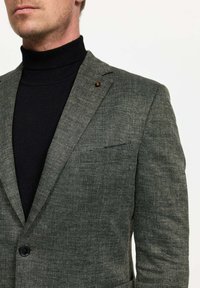 Blazer gris de espiga con solapas de muesca, cierre de un solo botón y un bolsillo en el pecho, superpuesto a un suéter de cuello alto negro.