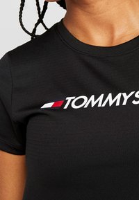 Black fitted t-shirt with a round neckline featuring the "TOMMY" logo in white and accents of red and blue on the left side.