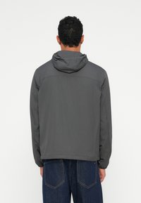 Szara bluza z kapturem o gładkiej fakturze, z szwem na górnej części pleców i elastycznymi mankietami. Noszona z ciemnoniebieskimi dżinsami.