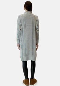 Grå stickad klänning med hög krage, med kabelstickade mönster och ribbad fåll. Matchad med svarta leggings och bruna ankelstövlar.