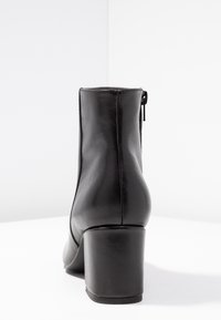 Schwarze Leder-Stiefelette mit runder Zehenpartie, seitlichem Reißverschluss und einem klobigen Absatz. Schlichte Textur und minimalistisches Design.