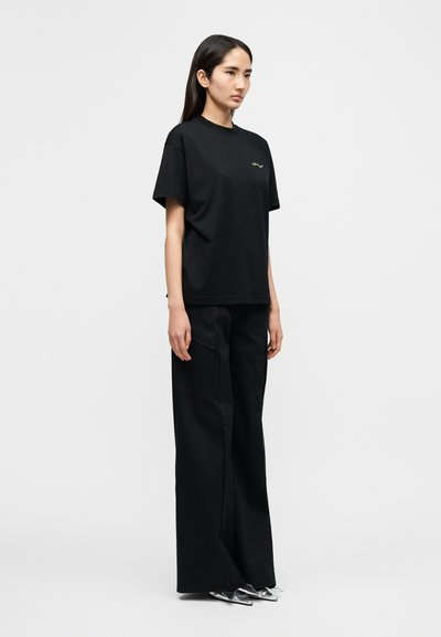 Μαύρο βαμβακερό t-shirt με άνετη εφαρμογή, κοντά μανίκια και διακριτικό λογότυπο. Συνδυασμένο με μαύρο παντελόνι με φαρδιά πόδια και πλαϊνές τσέπες.