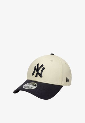 Gorra de béisbol con corona beige y visera negra, con el logo bordado en negro de los New York Yankees en el frente y un pequeño logo de la marca en el lateral.