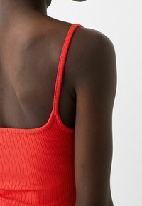 Débardeur rouge côtelé à fines bretelles, doté d'une surface texturée et d'une coupe ajustée, présentant un dos lisse et sans ornements.