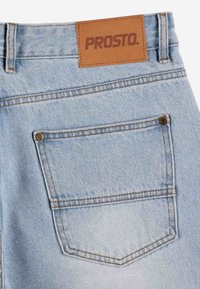 Jasnoniebieskie dżinsy z denimu z skórzaną metką wytłoczoną napisem "PROSTO". Posiadają tylną kieszeń z mosiężnym nitym detalem i kontrastowym szwem.