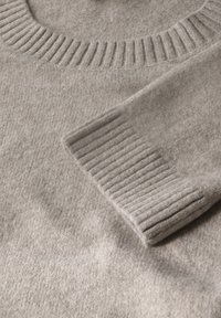 Lichtgrijze wollen trui met een geribbelde ronde halslijn en cuffs. Zachte textuur met een glad, gelijkmatig patroon over de stof.