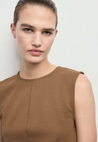 Bruine mouwloze top met een textuurafwerking, voorzien van een ronde halslijn en een schone, minimalistische stijl. Subtle naden detail in het midden.
