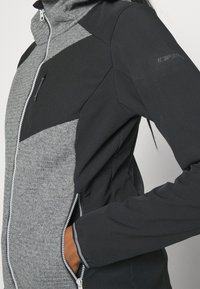 Veste zippée noire et grise avec un tissu texturé à l'avant, des manches lisses et une poche zippée sur la poitrine. Présente un col haut.